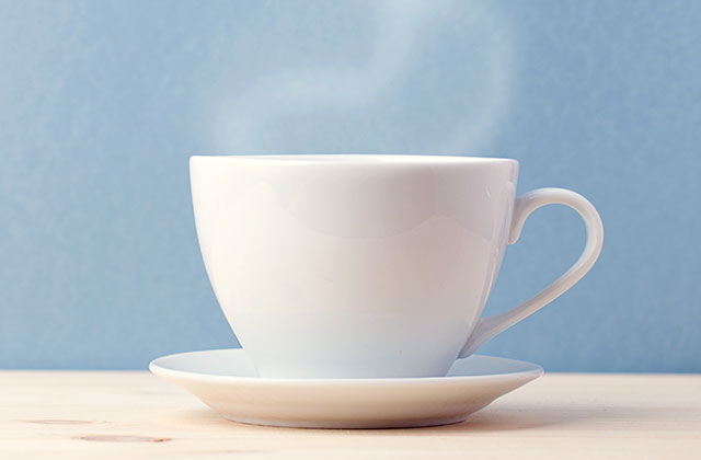 Weiße Kaffeetasse mit Untertasse dampft vor blauem Hintergrund auf heller Oberfläche