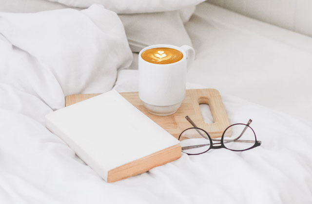 Cappuccino Latte-Art in weißer Kaffeetasse auf Holzbrett im Bett