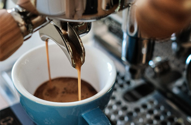frisch gebrühter Espresso fließt in eine blaue Kaffeetasse, die unter einer silbernen Siebträgermaschine steht