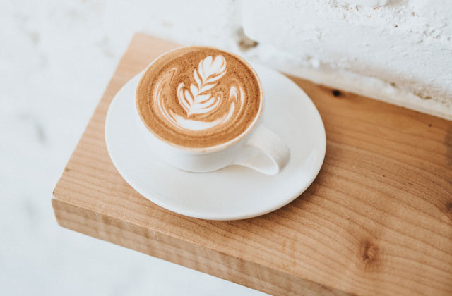 Latte-Art Cappuccino in weißer Kaffeetasse auf Holzbrett