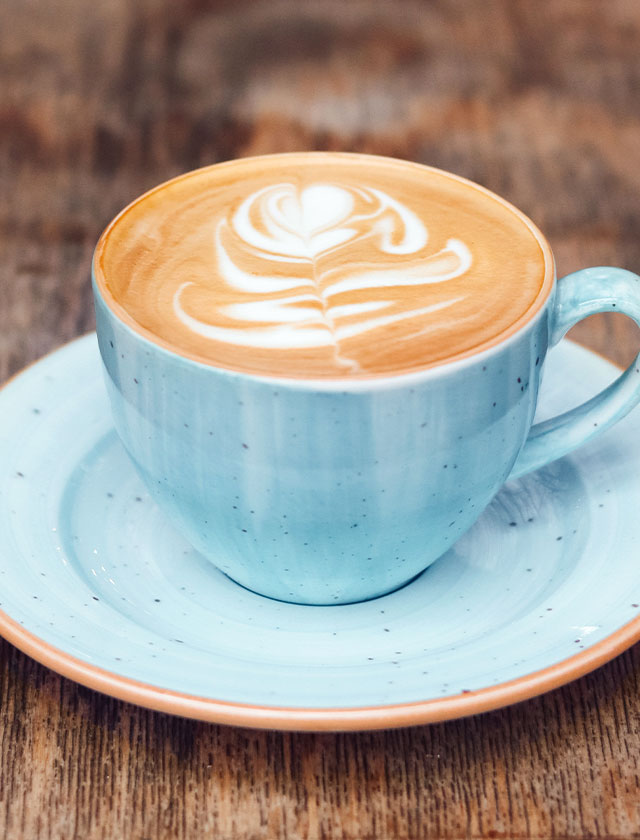 Cappuccino mit Latte-Art-Tulpe in hellblauer Tasse mit Untertasse auf brauner Holzfläche