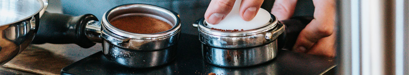 Barista-Hände tampen bei einem von zwei Siebträgern das Kaffeepulver 