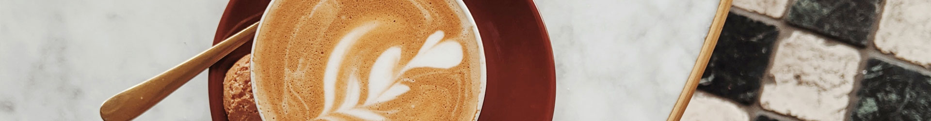 Latte-Art-Herz Cappuccino in Kaffeetasse auf roter Untertasse mit Keks und Teelöffel