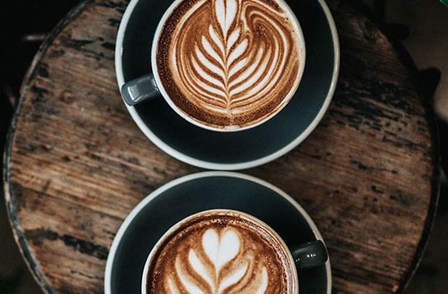 zwei Latte-Art-Blatt Cappuccini in schwarzen Tassen