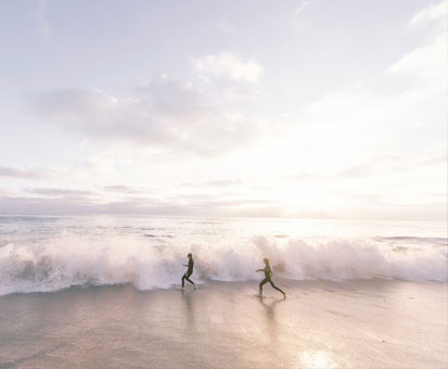 am Strand rennen zwei Personen zum Meer mit großen Wellen