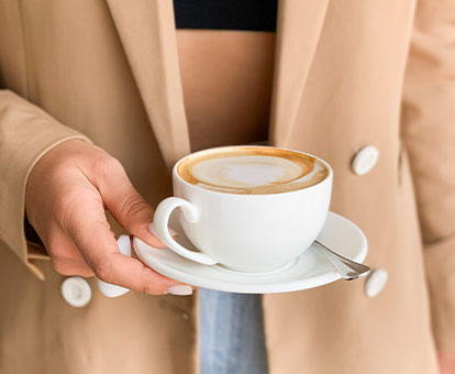 Frau hält Latte-Art-Herz Cappuccino in weißer Tasse