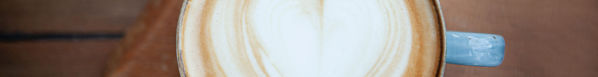 Latte-Art-Herz Cappuccino in blauer Tasse auf brauner Holzfläche