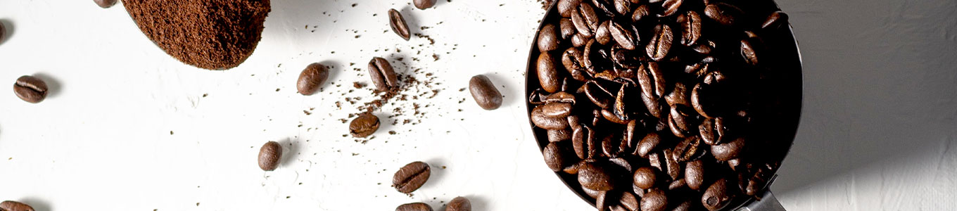 Schale mit Kaffeebohnen und Löffel mit gemahlenem Kaffee auf weißem Untergrund