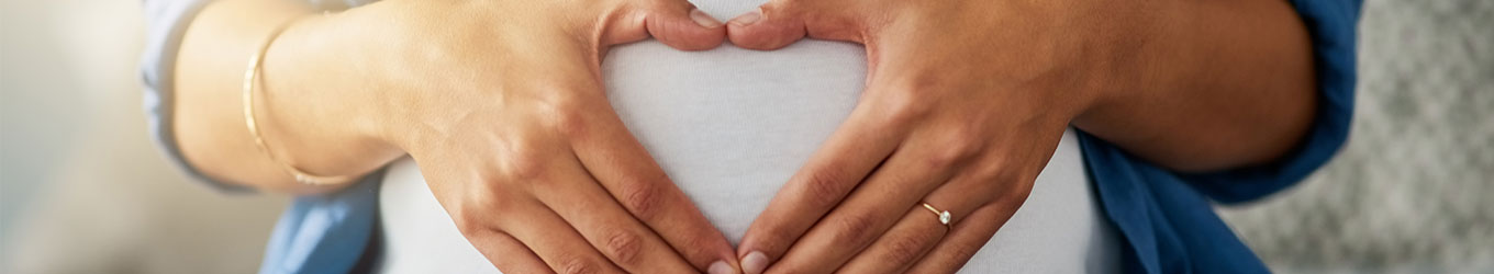 schwangere Frau formt mit ihren Händen ein Herz auf ihrem Bauch