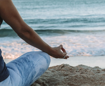 Person in blauen Shorts meditiert im Schneidersitz am Strand